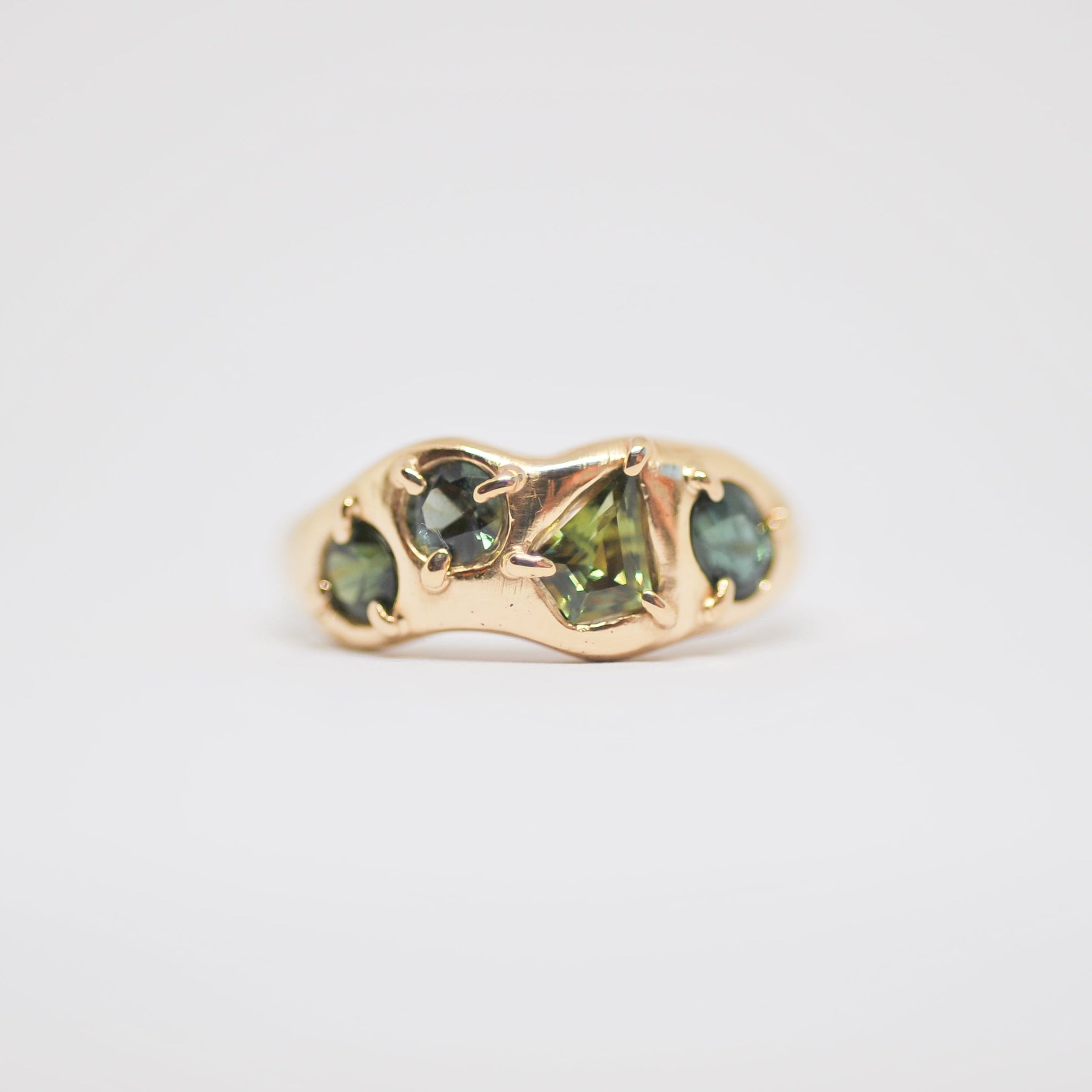 Gold ring with green gemstones on a light gray background